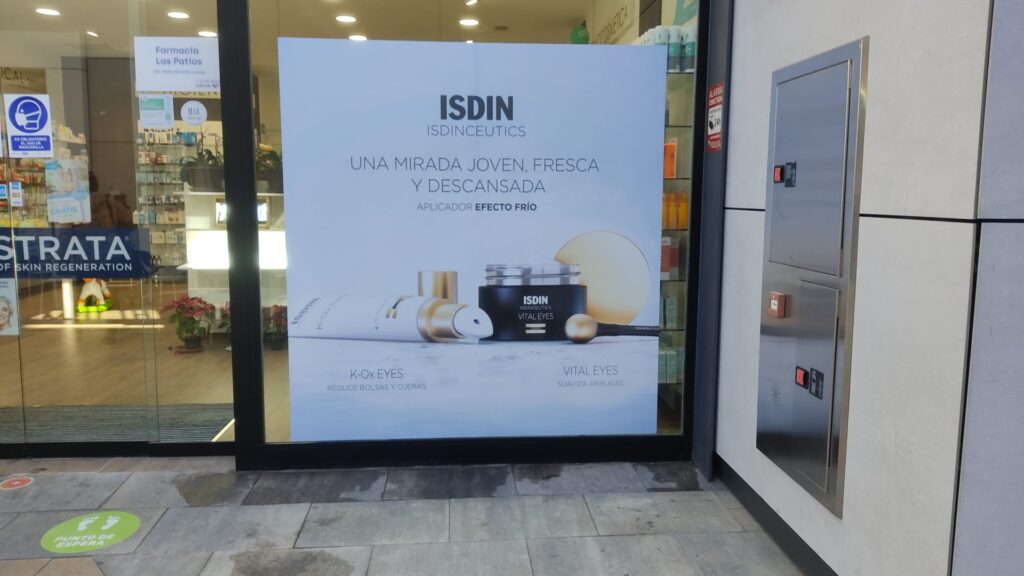 La imagen muestra un vinilo en el exterior de una tienda de ISDIN.