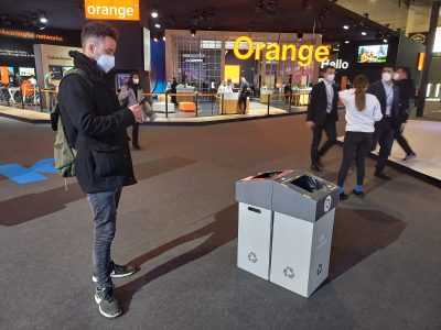 La imagen muestra a una persona enfrente del estand de Orange de MWC Barcelona con el móvil.